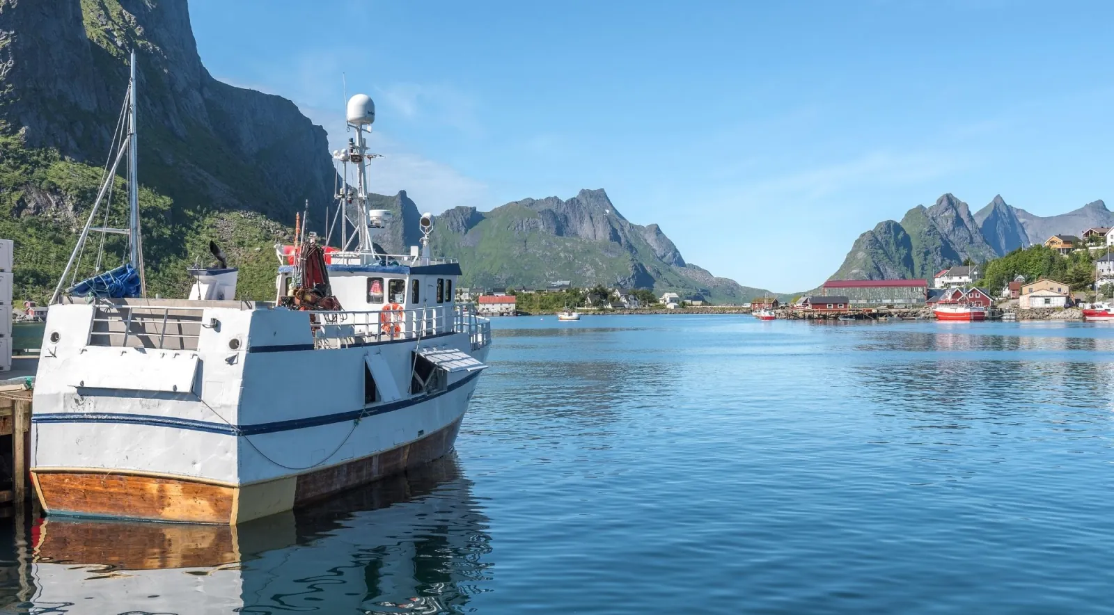 A white fishing boat moored in the calm harbour of Reine under blue summer skies