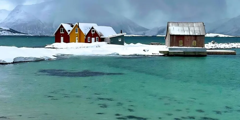 Snow-dusted fishing cabins on turquoise water at Sommarøy near Tromsø