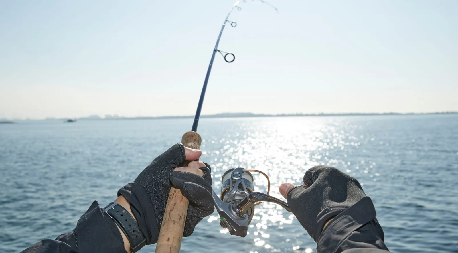 First-person view of hands working a rod and reel over sunlit open sea